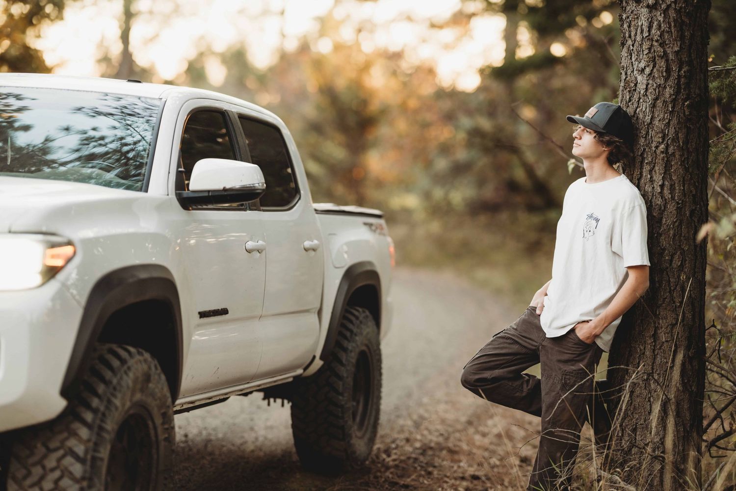 A senior leaning against a tree with his white truck close by, looking off into the distance, captured by a Walla Walla photographer.