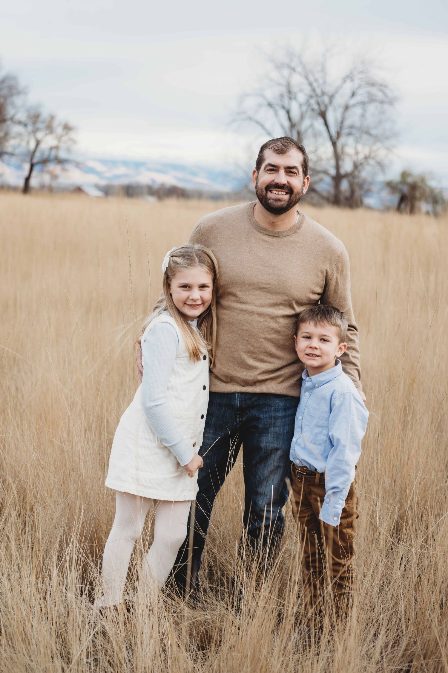 A dad with his two children hugging and looking at the camera.