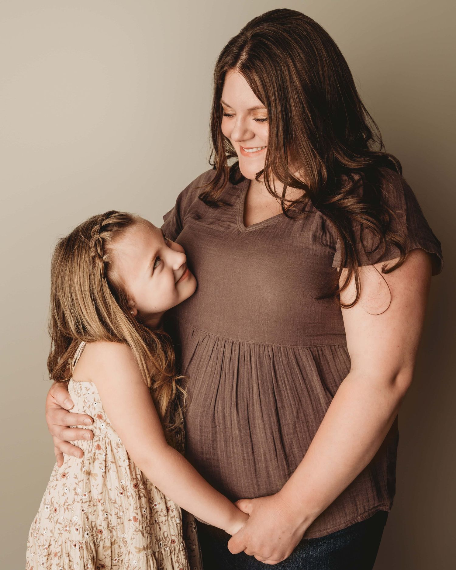 A mom and her daughter hold hands and look at each other smiling for a portrait.