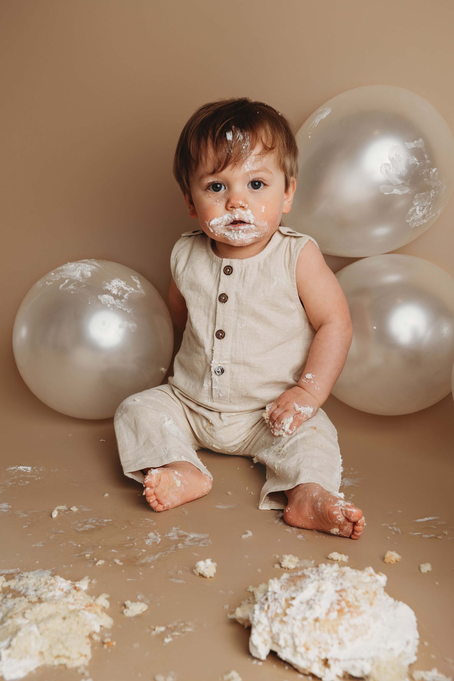 A portrait of a one year old boy wearing neutral tones covered in white frosting.