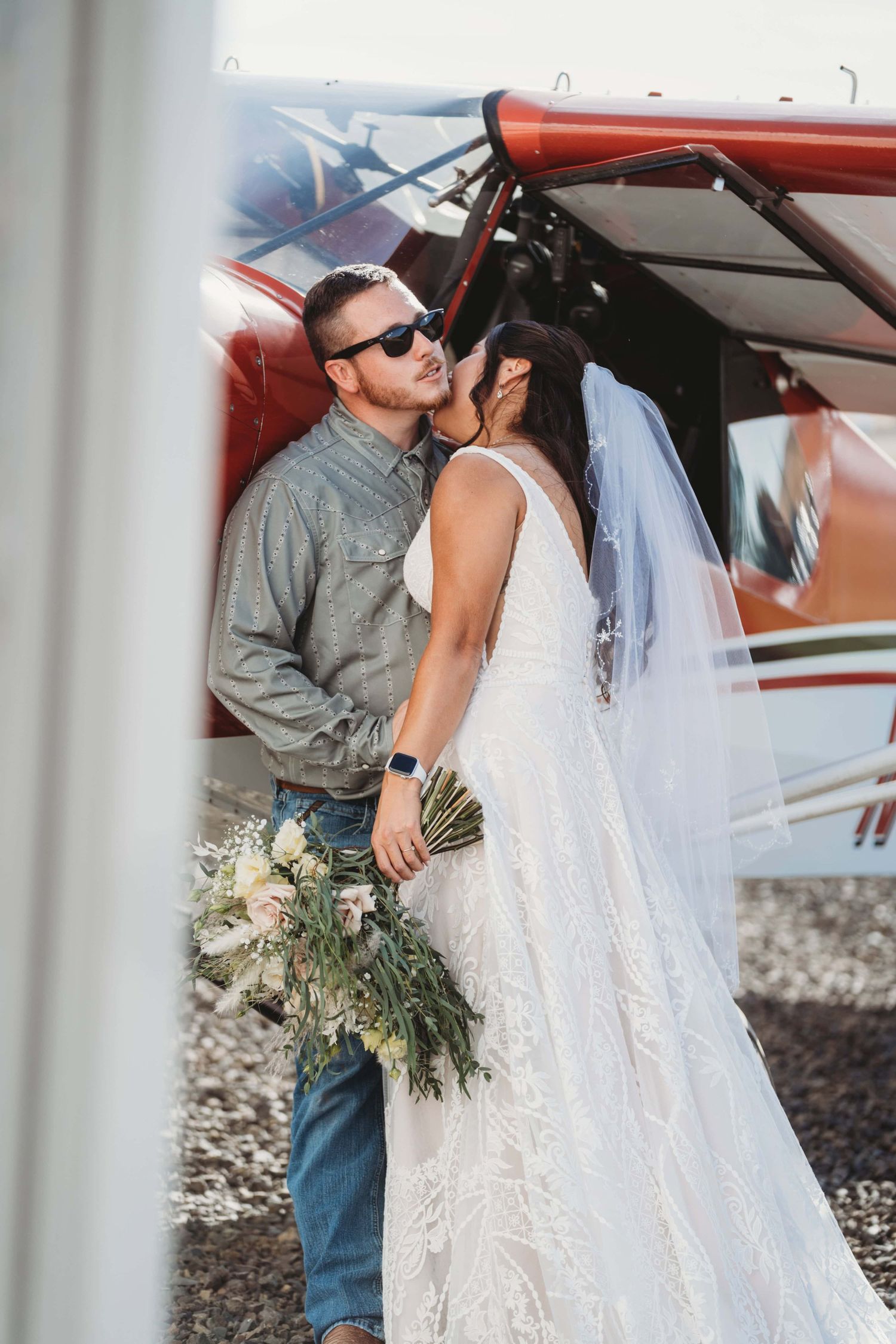 A bride and groom kissing while standing against their private plane after their wedding ceremony.