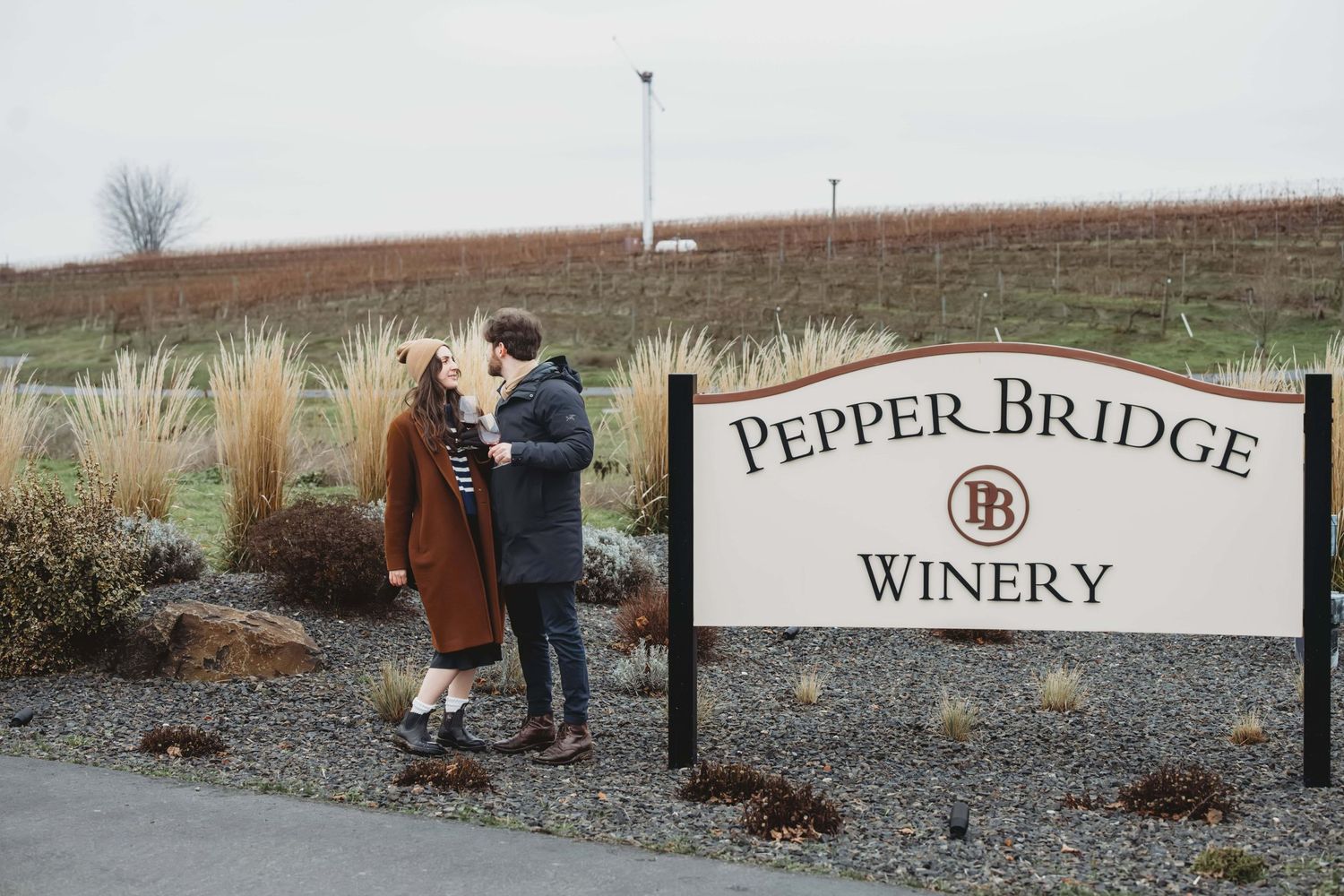A couple standing next to the Pepperbridge Winery sign in Walla Walla just after getting engaged.