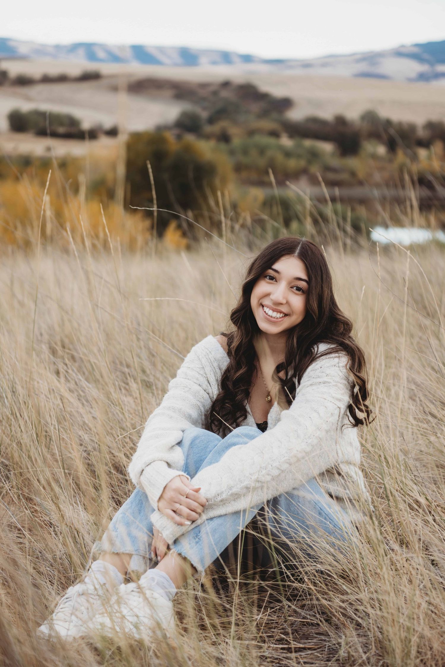 A young woman sitting in a field with a lake and rolling hills in the background at Bennington Lake in Walla Walla.