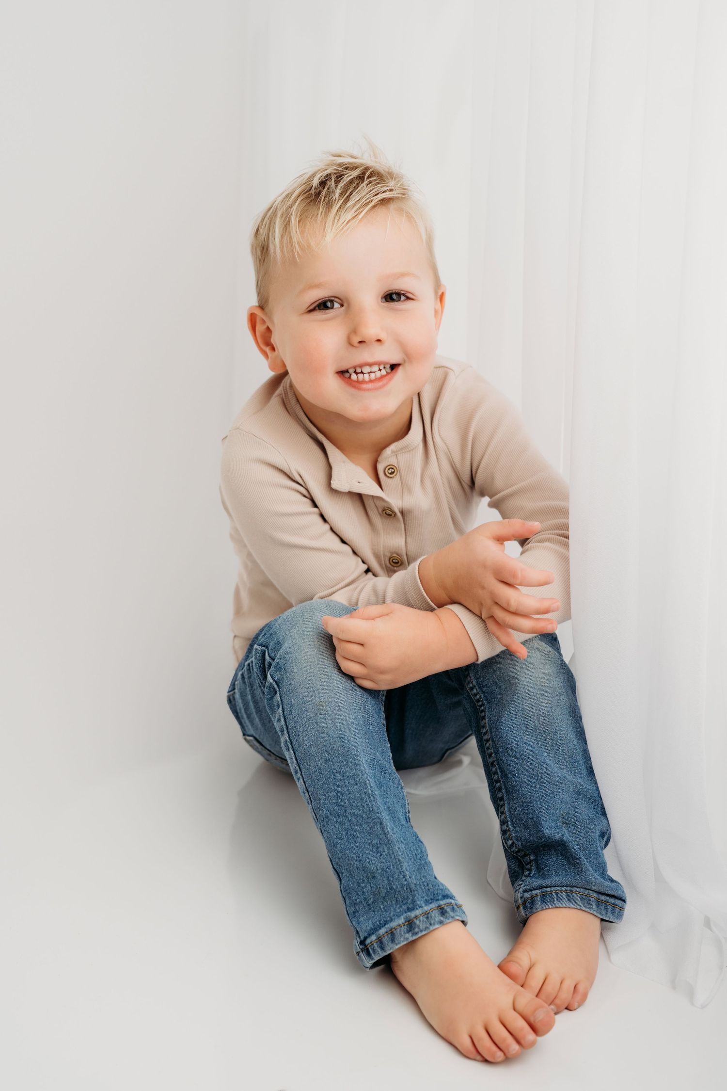 A classic studio portrait of a boy sitting with his knees up on a white backdrop in Walla Walla.