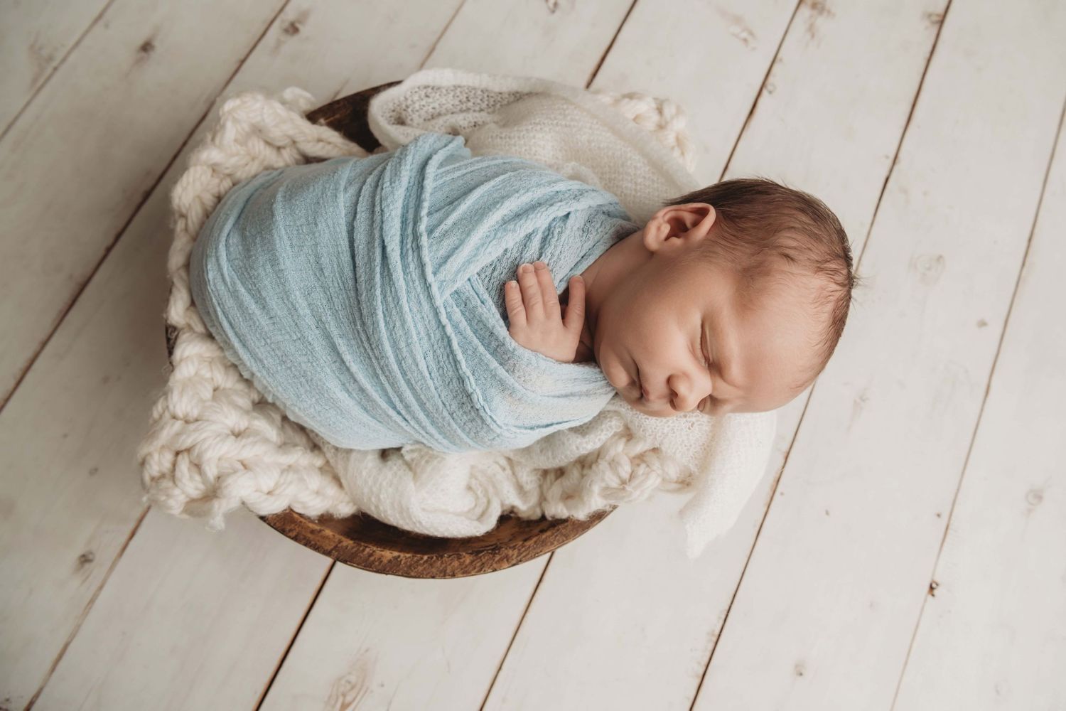 Newborn baby laying in a wooden bowl wrapped in blue in Walla Walla studio