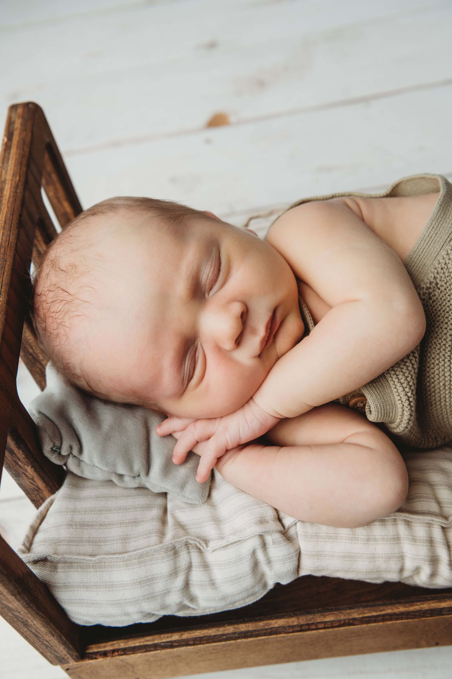 Newborn baby boy laying on a pillow on a wooden bed at a Walla Walla portrait studio.