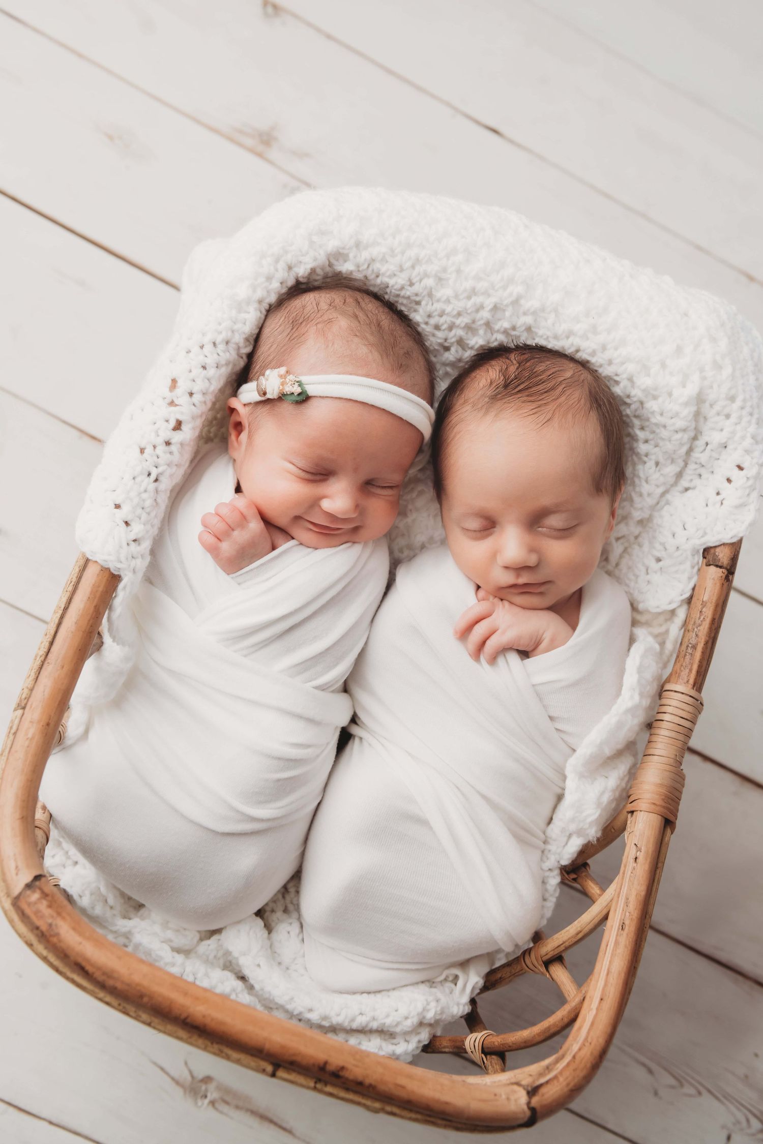 Newborn twins lay in a boho bassinet wrapped in white at a Walla Walla photography studio.