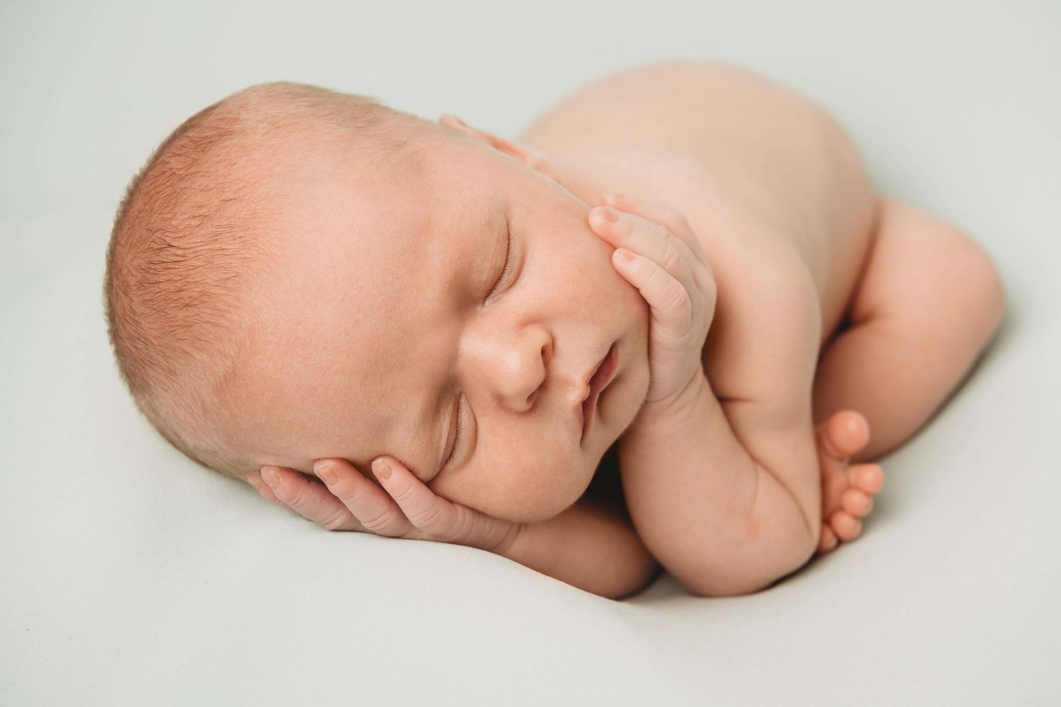 A newborn sleeping with his hands near his face on a light blue blanket.