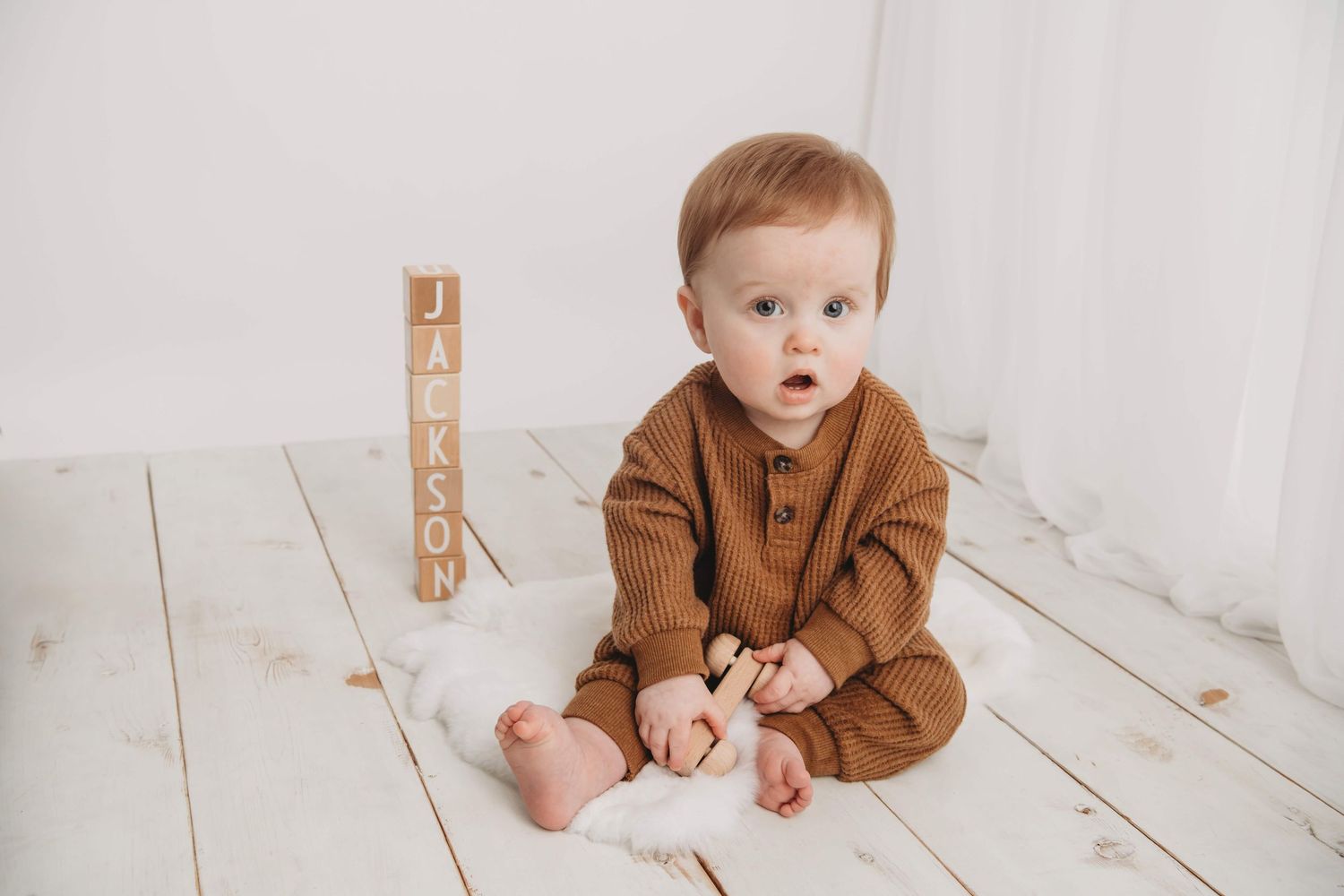 A baby boy wearing brown on an all white backdrop with wooden blocks spelling out his name at a Walla Walla photography studio.