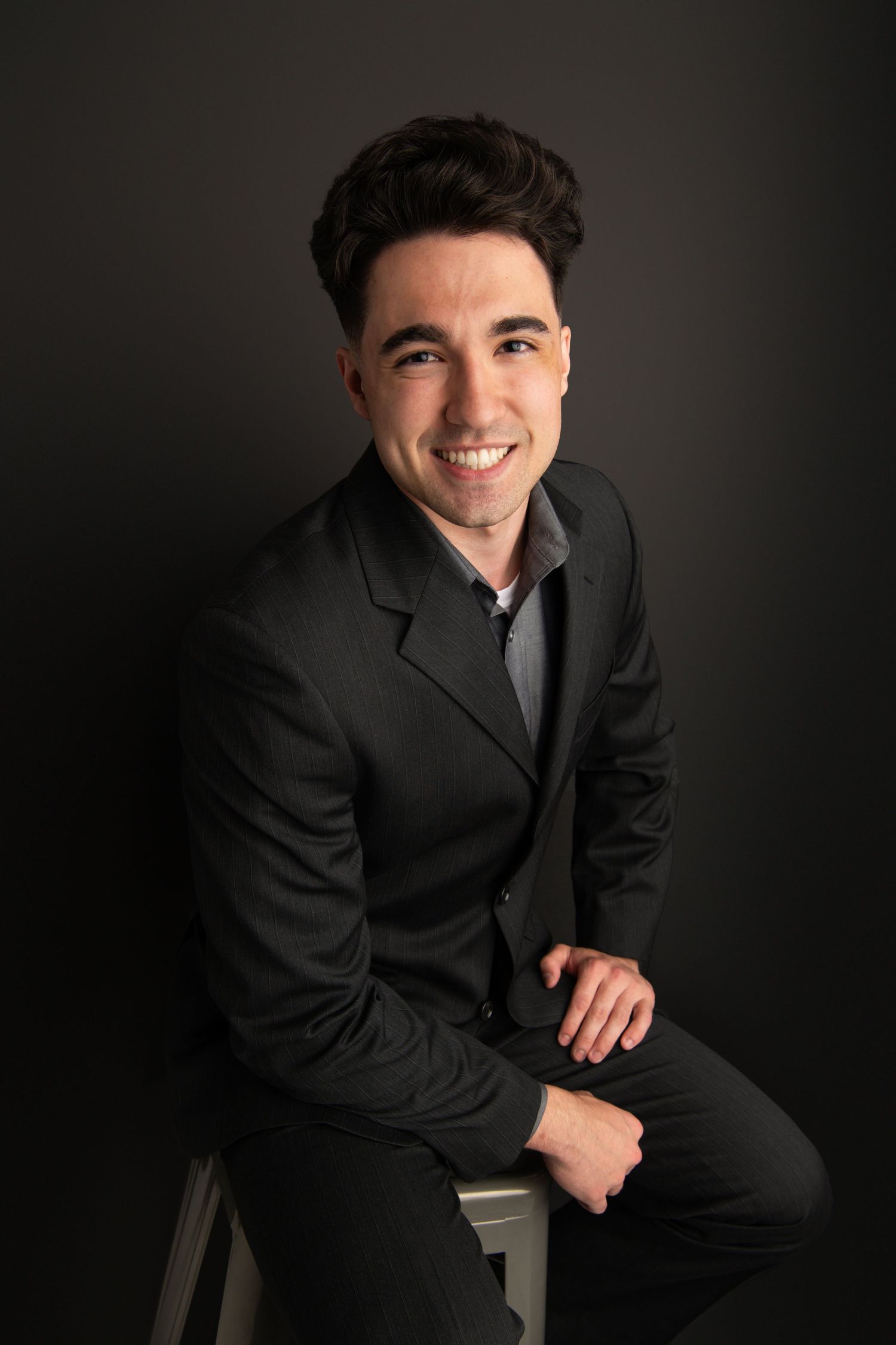 A headshot of a man on a black backdrop wearing a dark suit.
