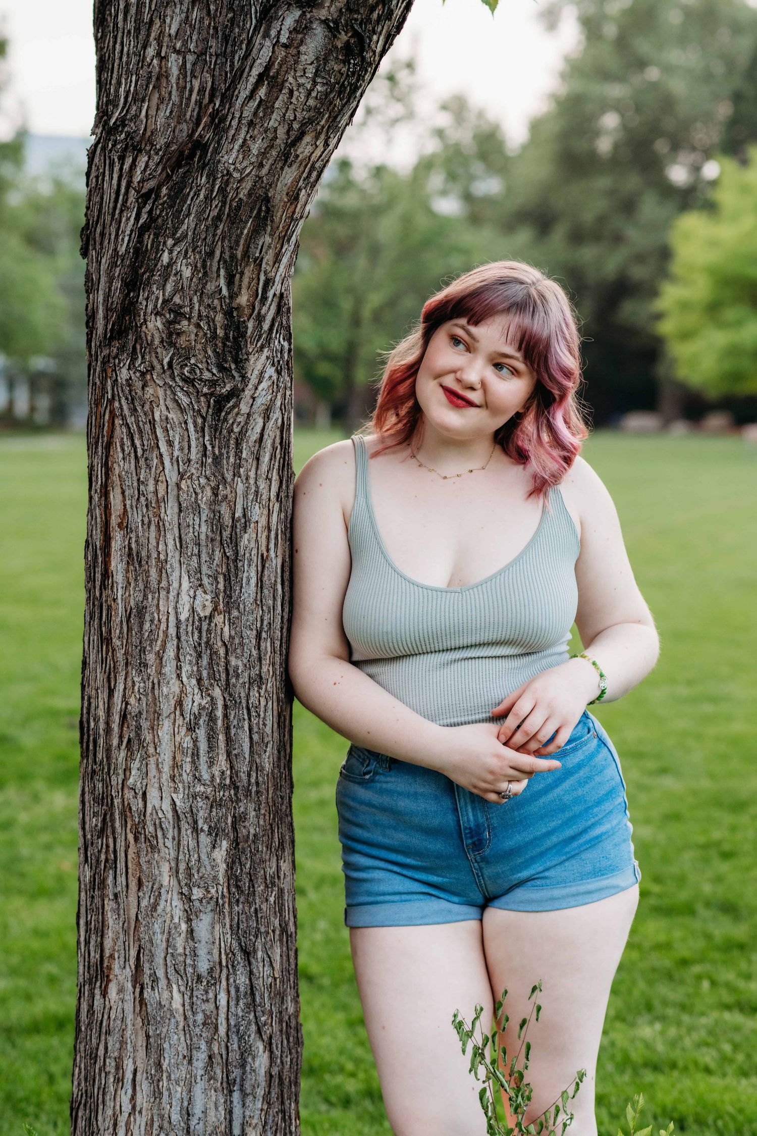 A Walla Walla Community College graduate leaning against a tree and smiling for her senior portrait session.