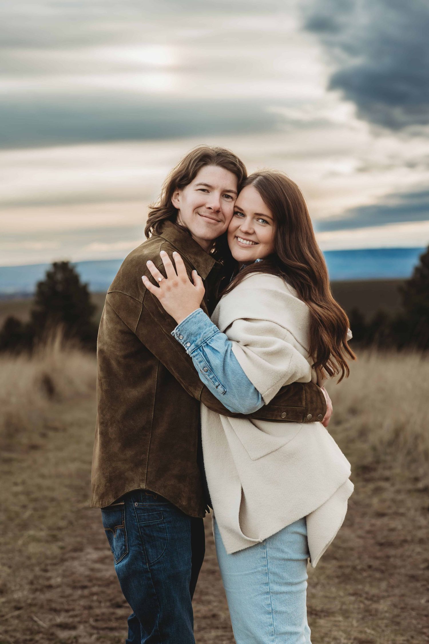A newly engaged couple hugging with stormy skies.
