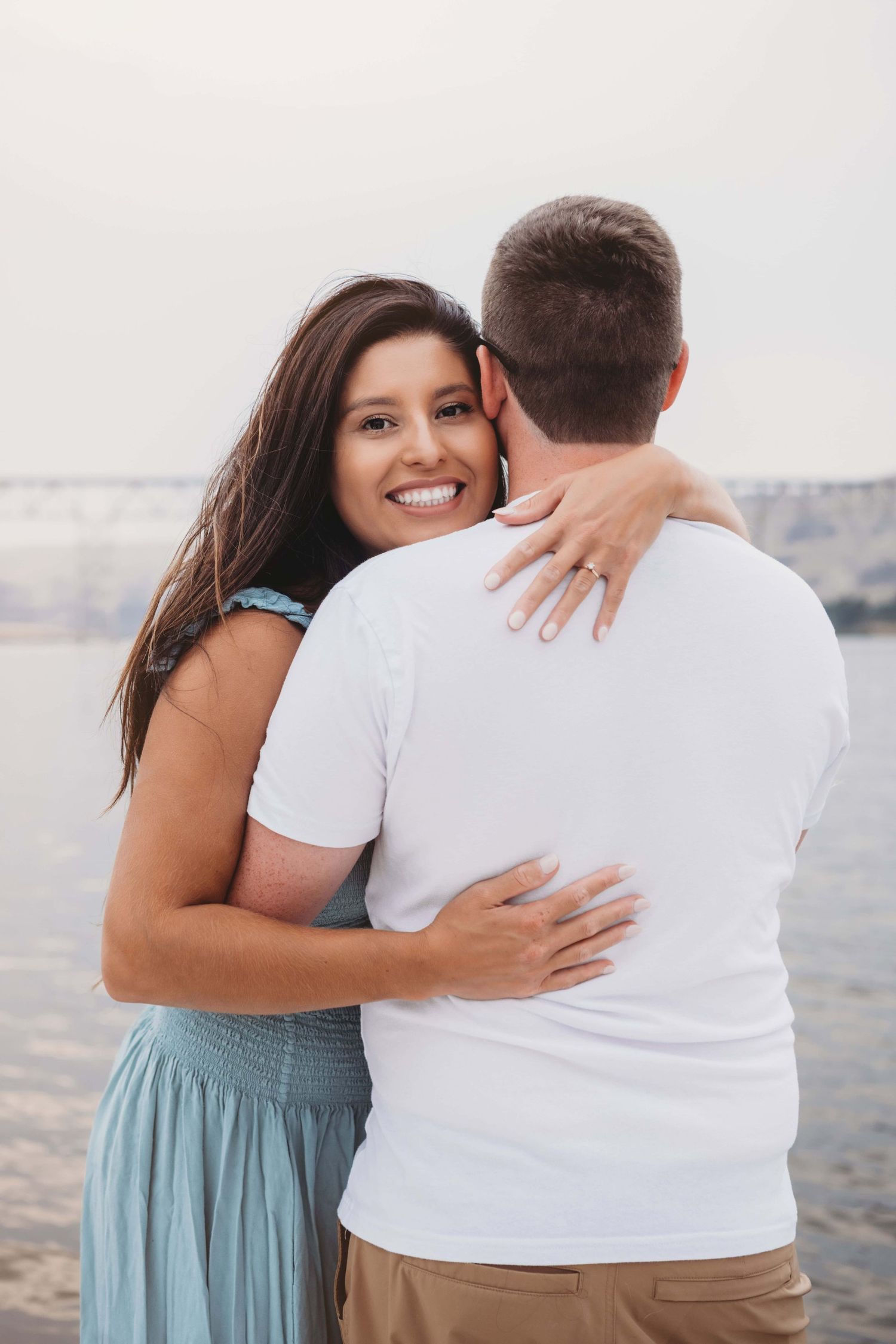 A woman hugging her fiancé wearing a blue dress on their boat in the Columbia river.