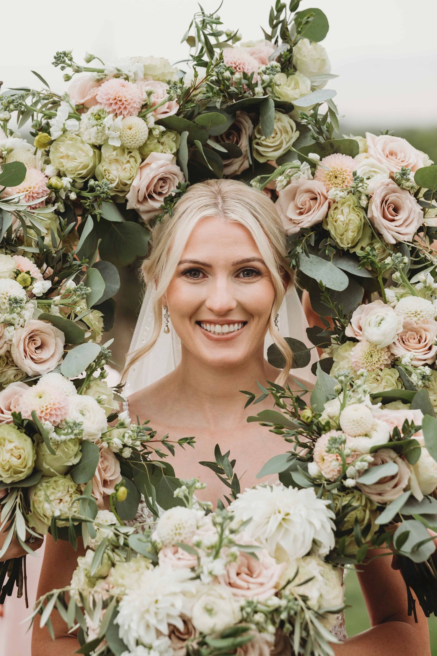 A portrait of a bride surrounded by pink and cream colored floral bouquets on her wedding day.