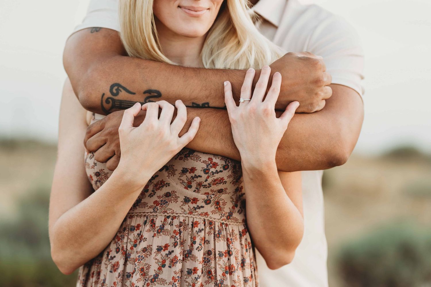 A close up of a mans arms wrapped around his fiancé and her holding onto his arms.
