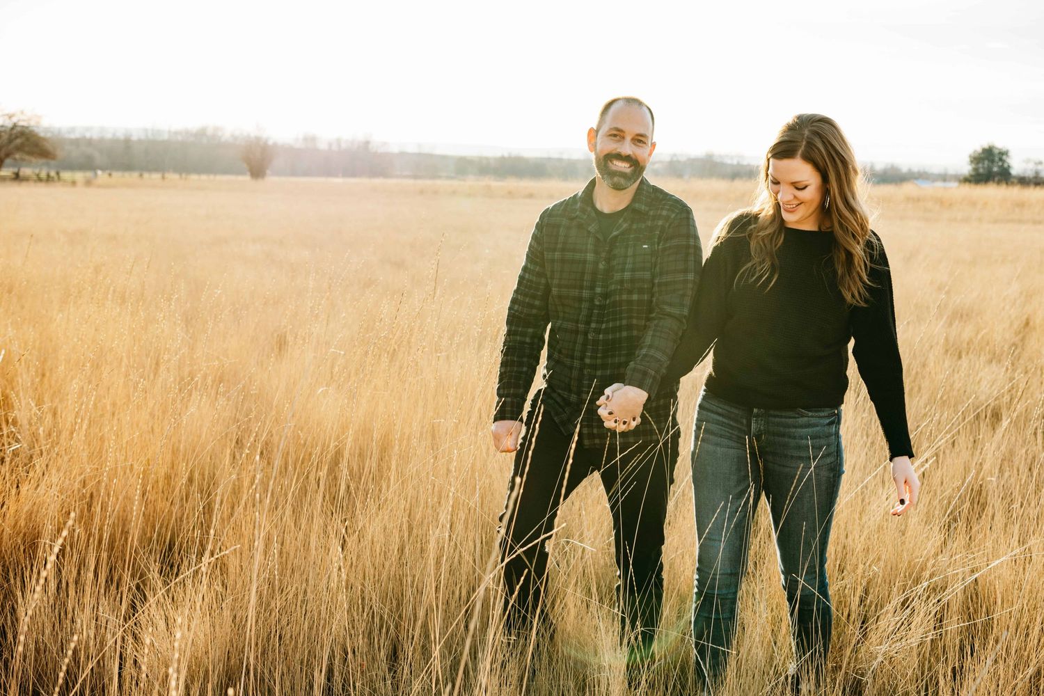 A couple wearing all black walking through a tall golden field.