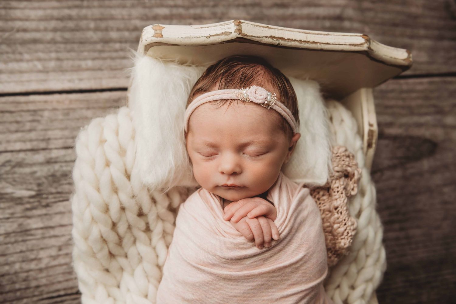 Newborn girl sleeps on a white pillow in a vintage wooden bed.