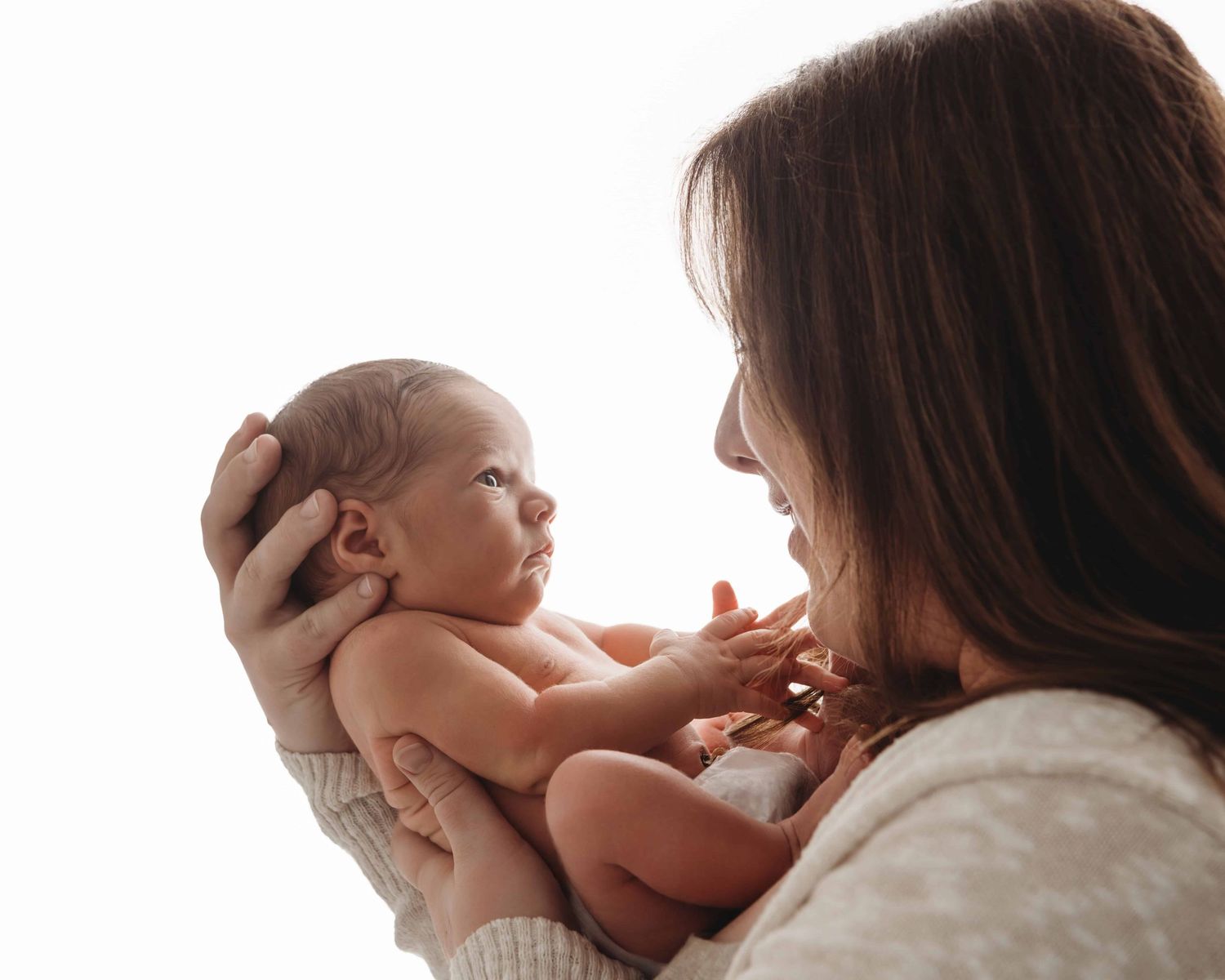A backlit portrait of a mother and her newborn baby looking at each other.