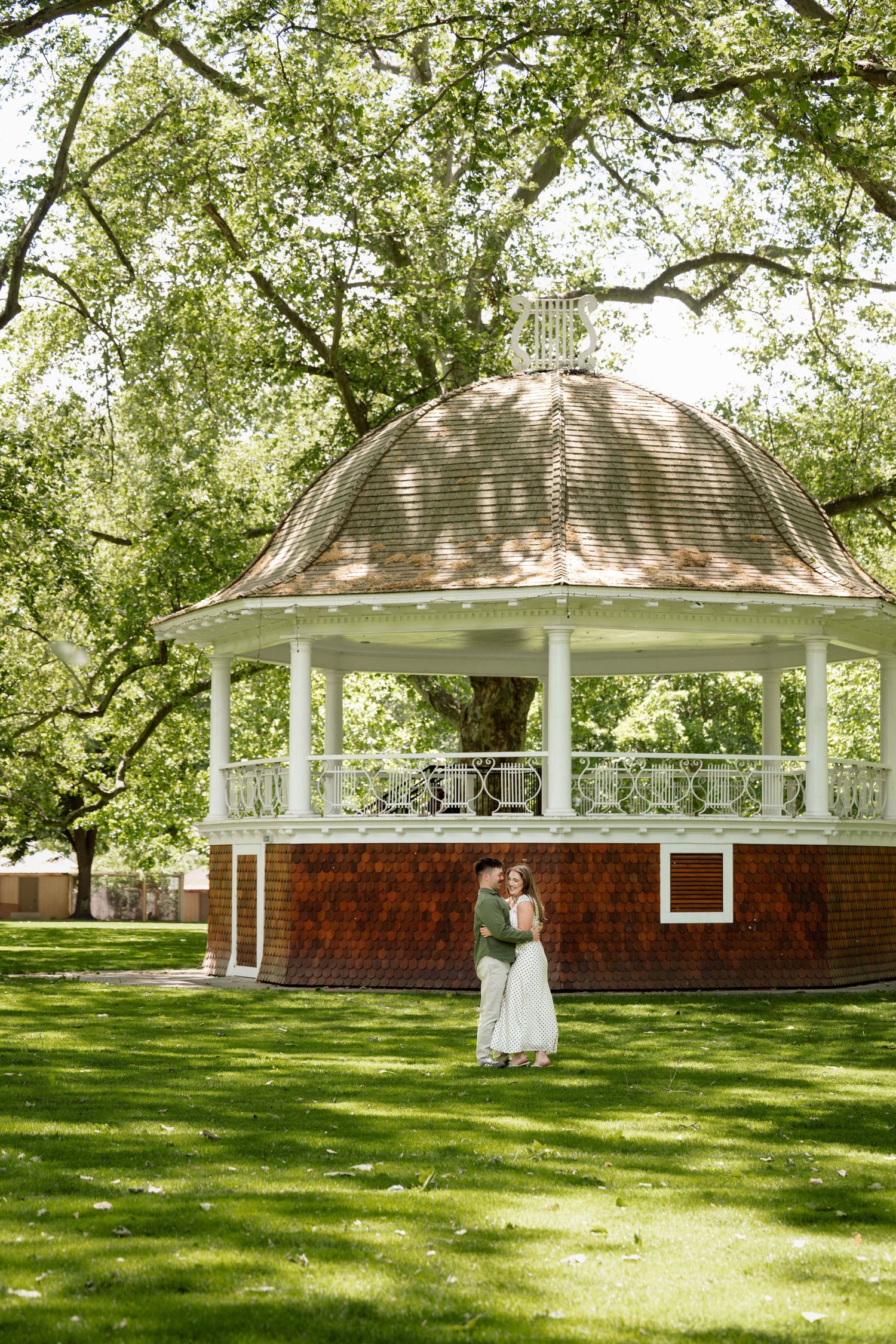 A couple embracing in front of a gazebo at a park.