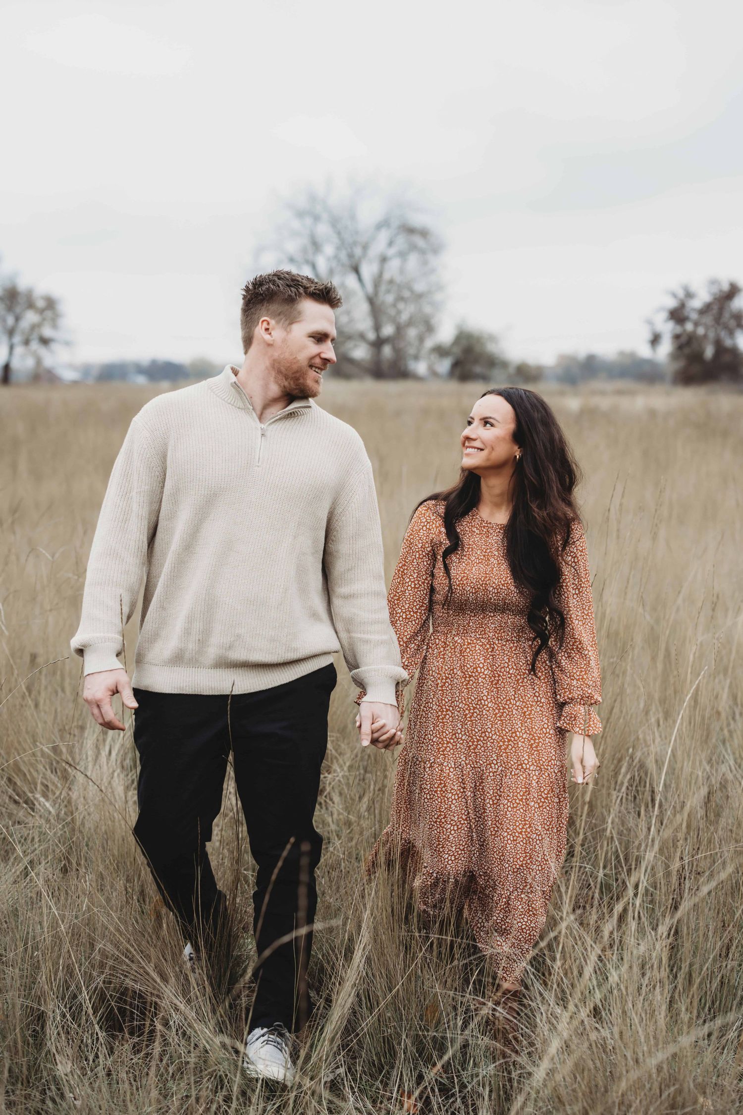 A couple looking at each other and smiling as they walk through tall grasses.