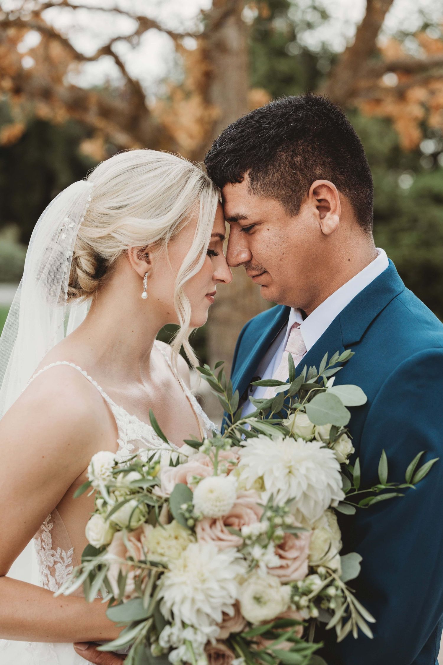 A close up portrait of a bride and groom touching foreheads with a cream and blush bridal bouquet.