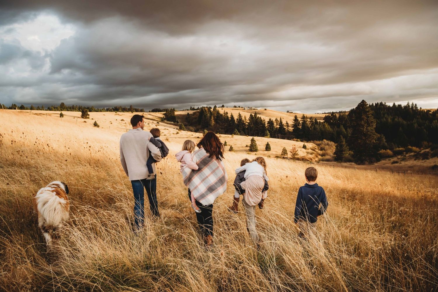 A family walks through a field during sunset with their large dog.