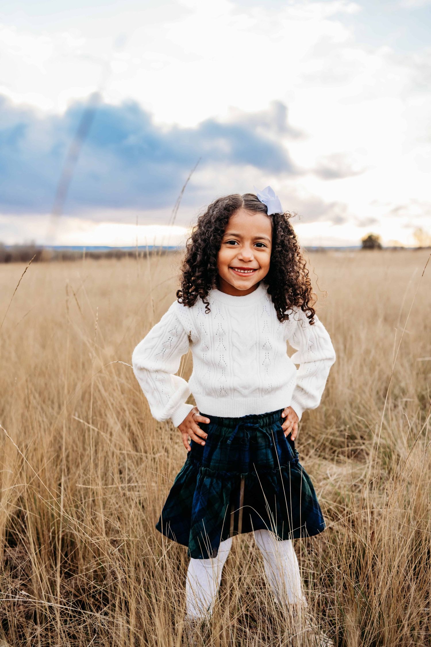 A child standing in a field with her hands on her hips during sunset.