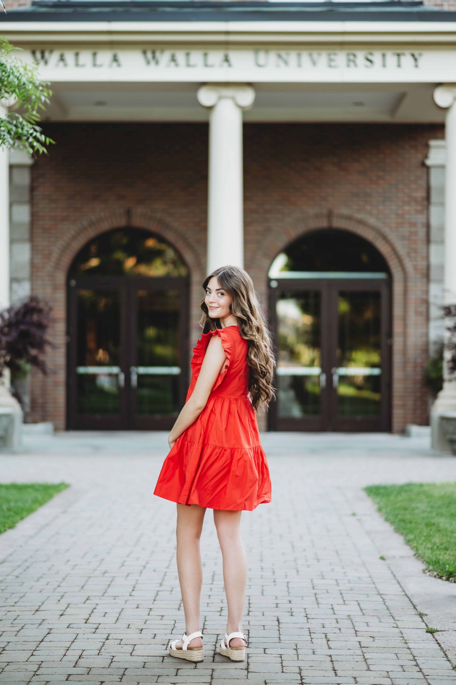 A portrait of a senior wearing a red dress with the Walla Walla University building in the background.