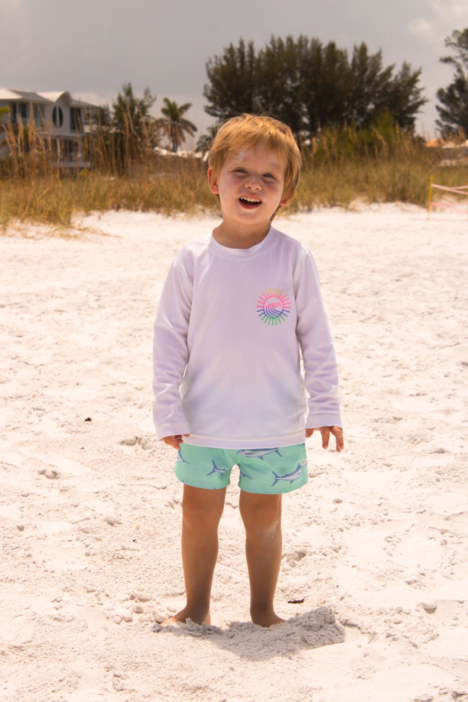 A toddler wearing a white sweatshirt and mint shorts plays in pristine beach sand.