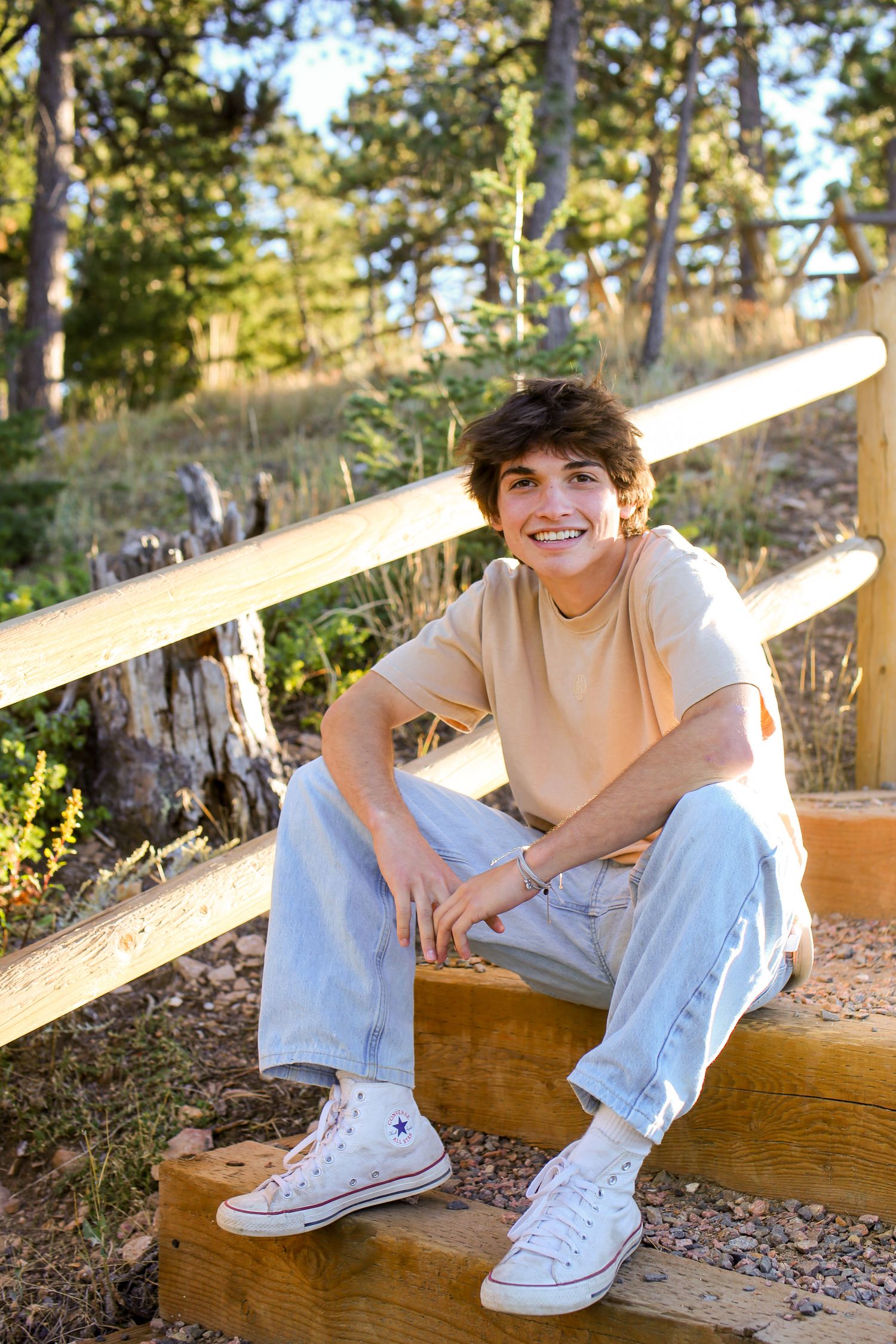 Person relaxing outdoors on wooden bench wearing casual attire and white sneakers in natural setting.