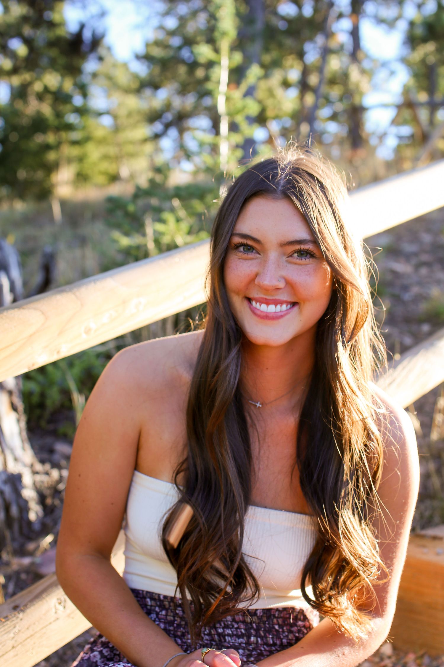 Person in white top and floral skirt poses on wooden deck with forest backdrop.