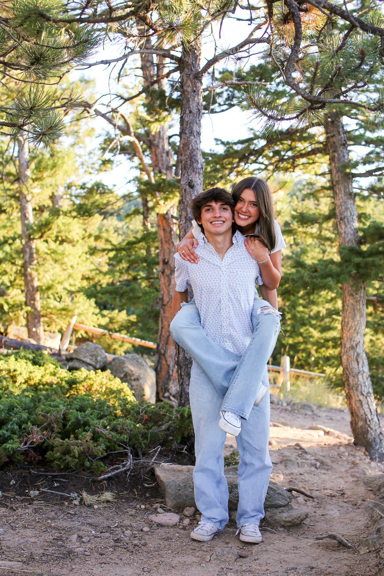 Couple enjoying playful moment on mountain trail surrounded by pine trees.