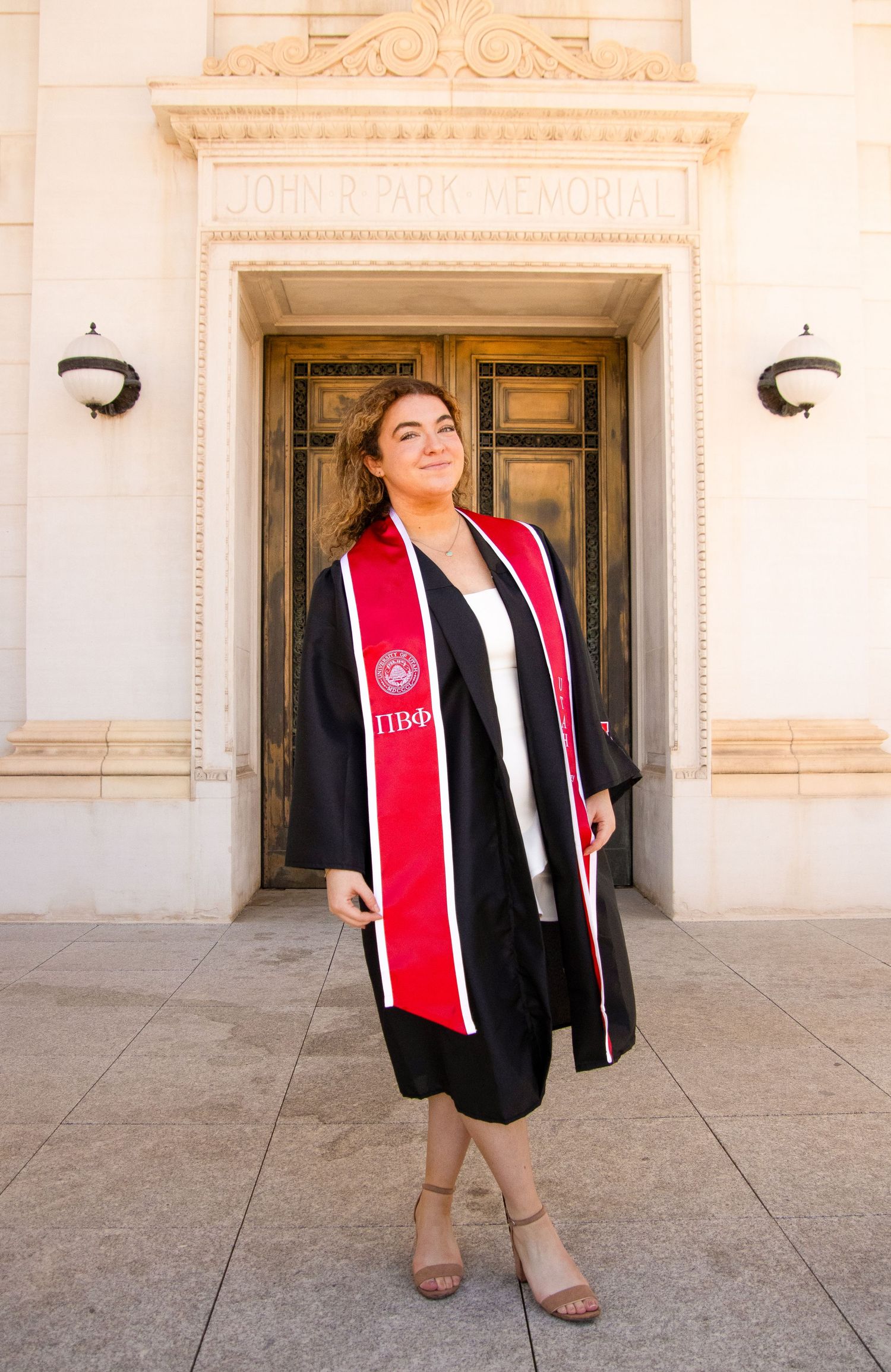 Graduate wearing Pi Beta Phi stole poses joyfully in front of classical architecture.