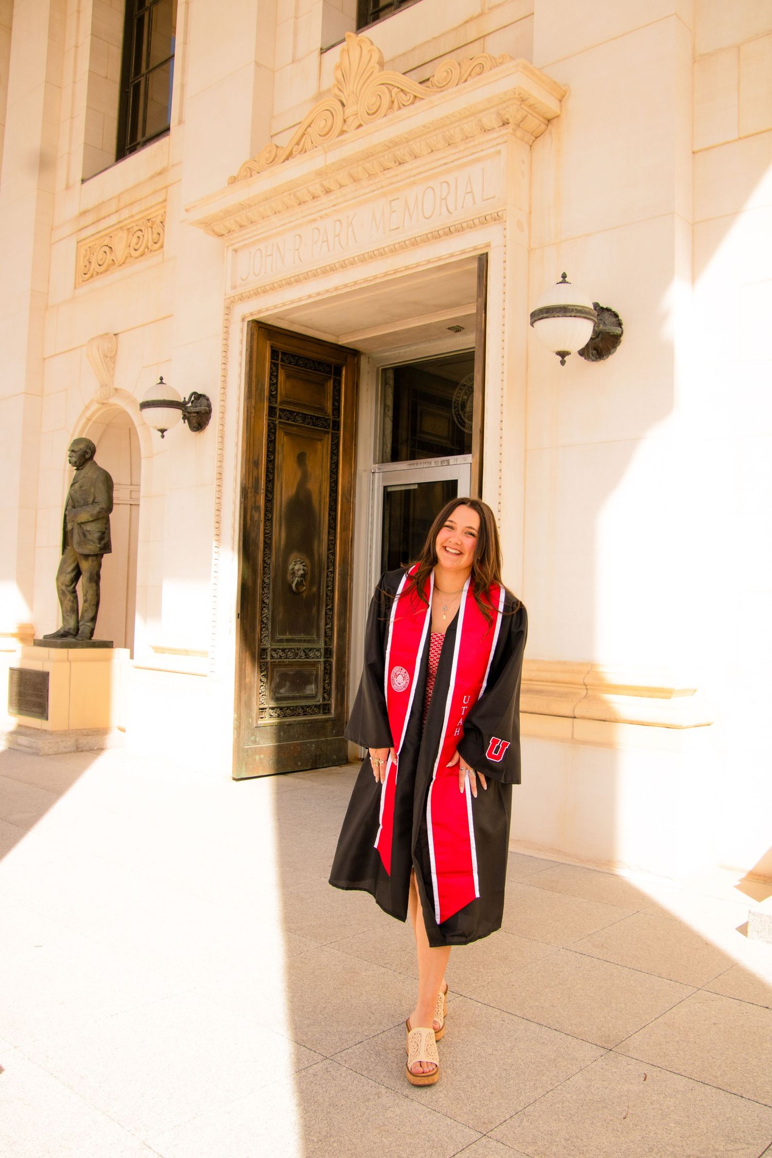 Graduate walking along ornate white building exterior with classical architectural details.