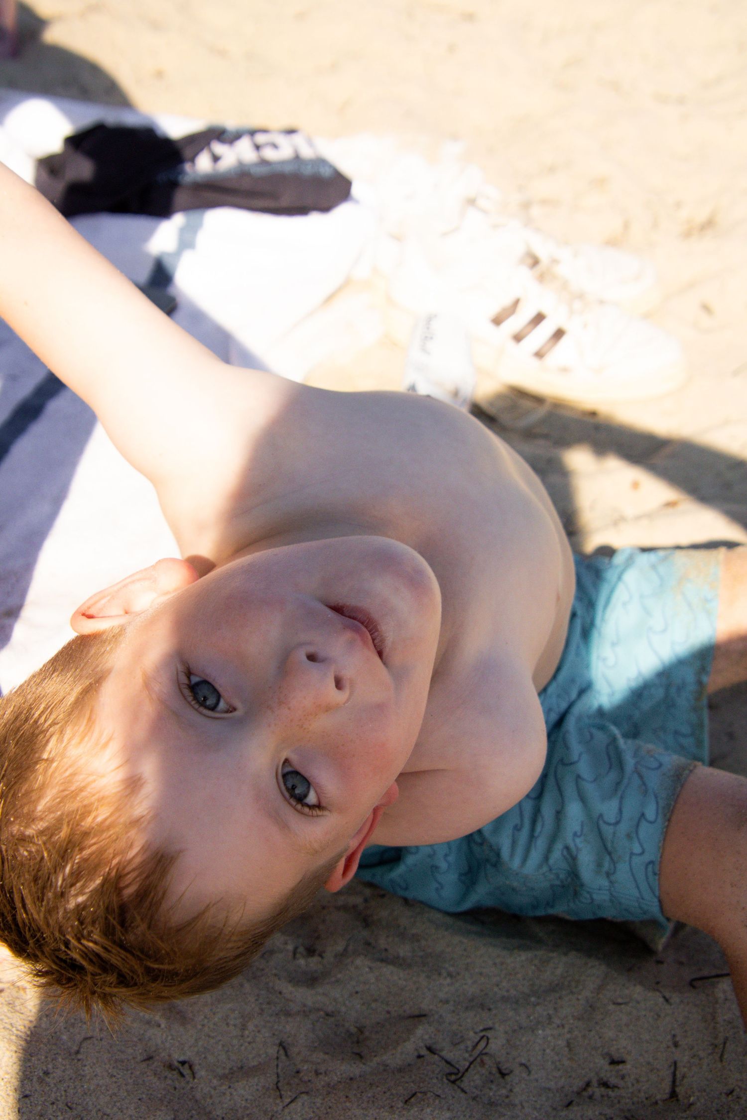 Close-up portrait of someone lying on sand at the beach in warm sunlight.