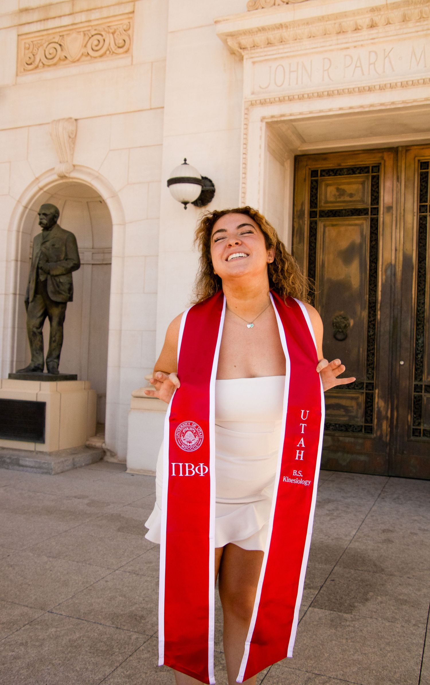 Graduate celebrates with red sorority stole in front of historic building entrance.