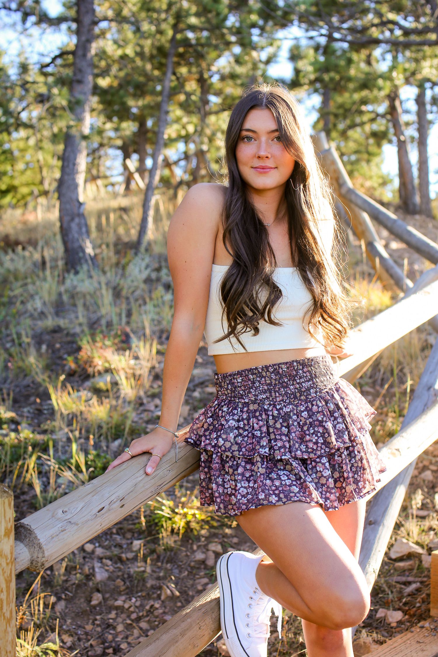 Person in summer outfit poses on wooden fence with forest background.