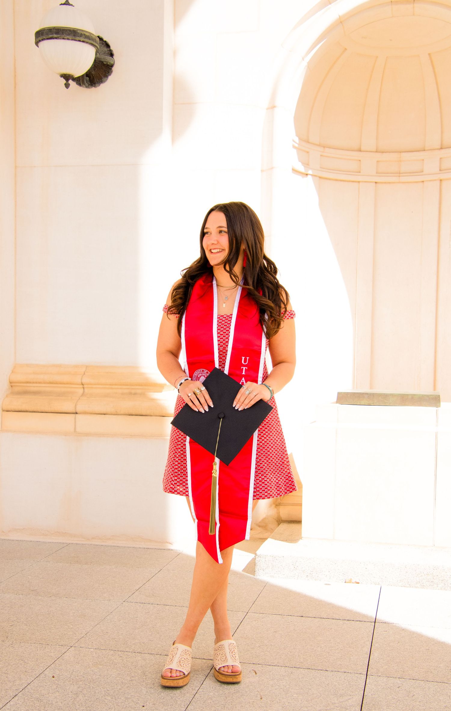 Graduate in red stole strikes various poses along white columned building facade.