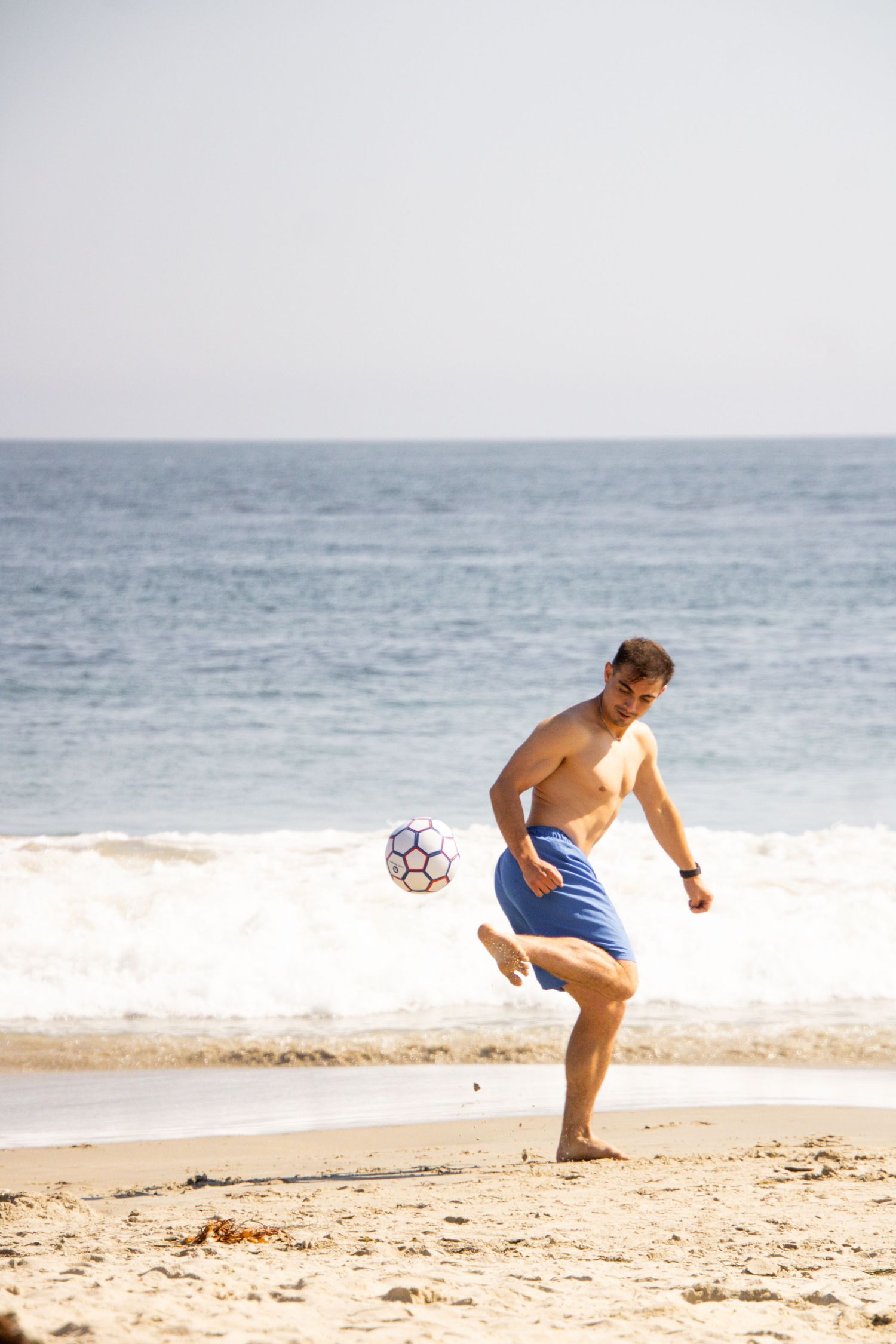 Someone kicks a soccer ball while enjoying a beach day by the ocean.