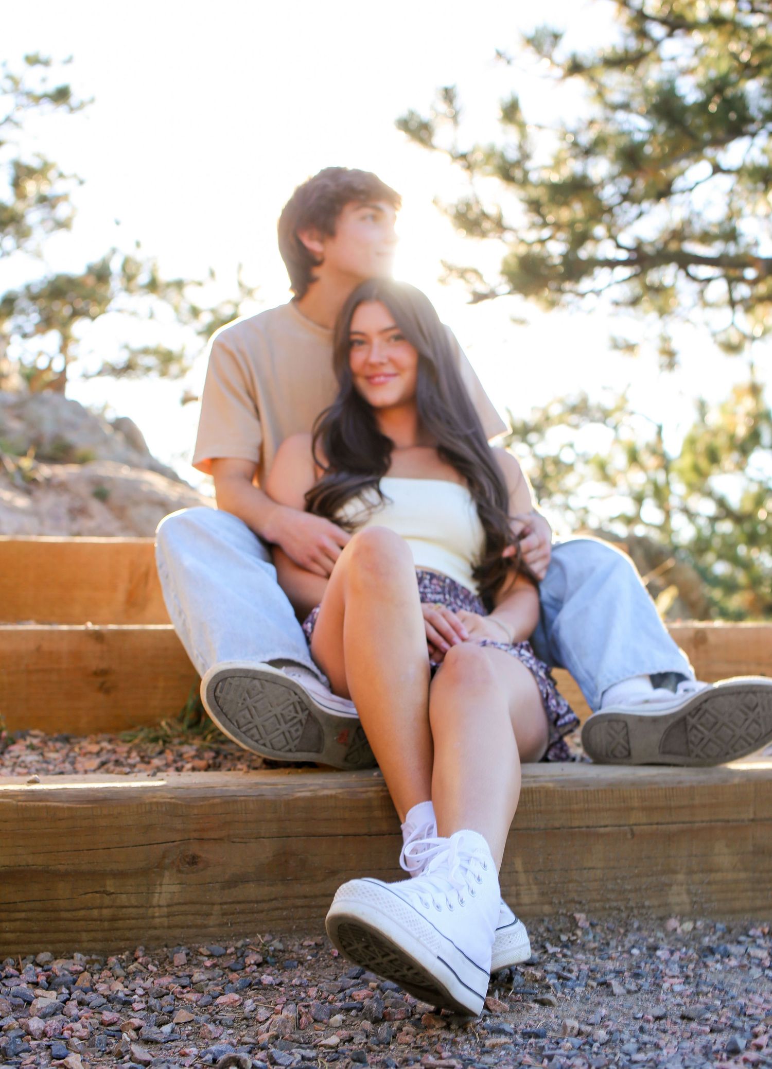 Couple relaxing on wooden bench during golden hour with pine trees in background.