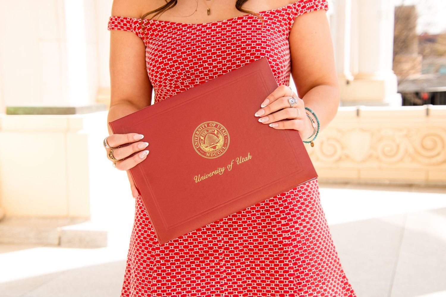 Person in a red polka dot dress holding graduation documents.