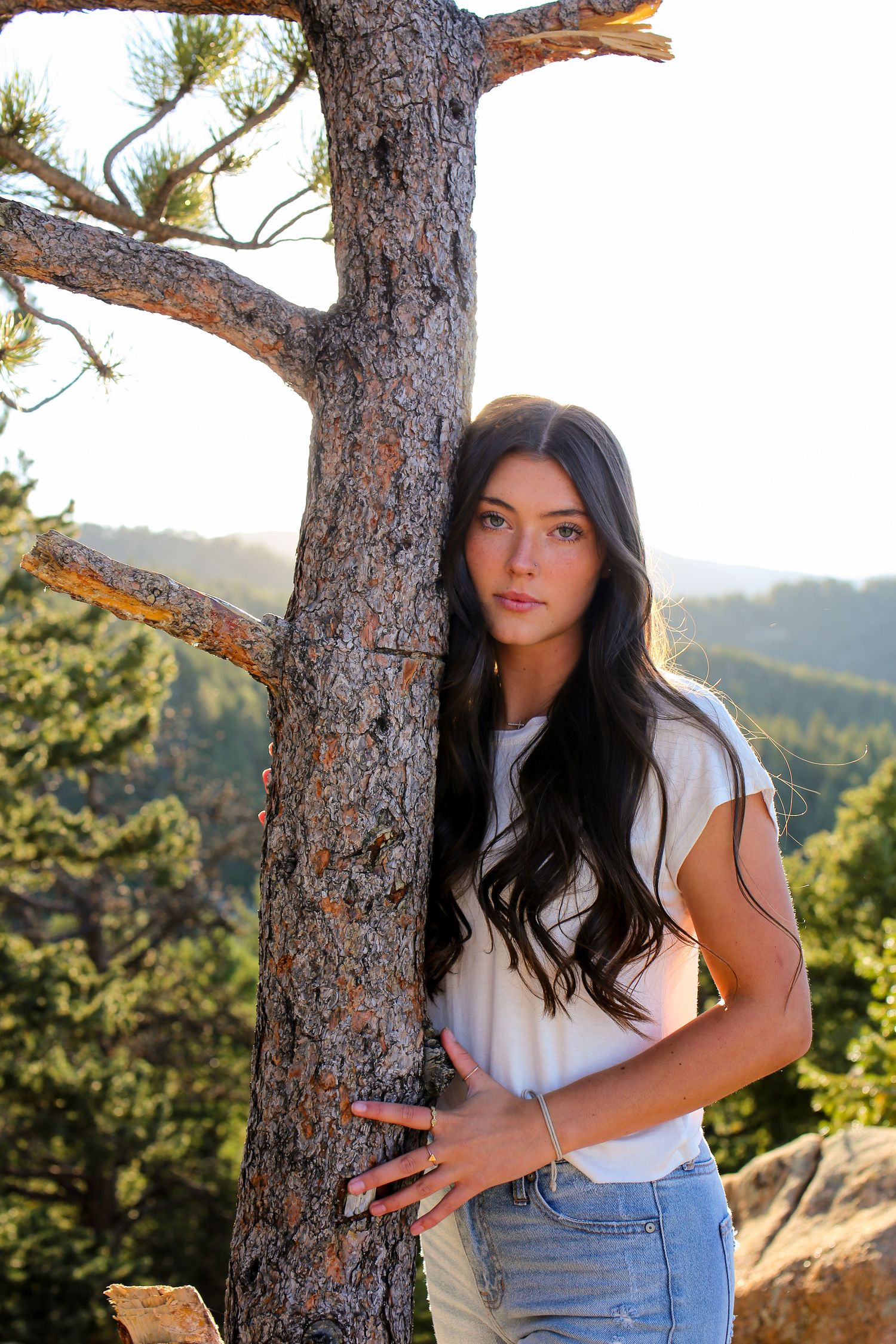 Portrait session in nature with pine trees and mountain backdrop during golden hour.