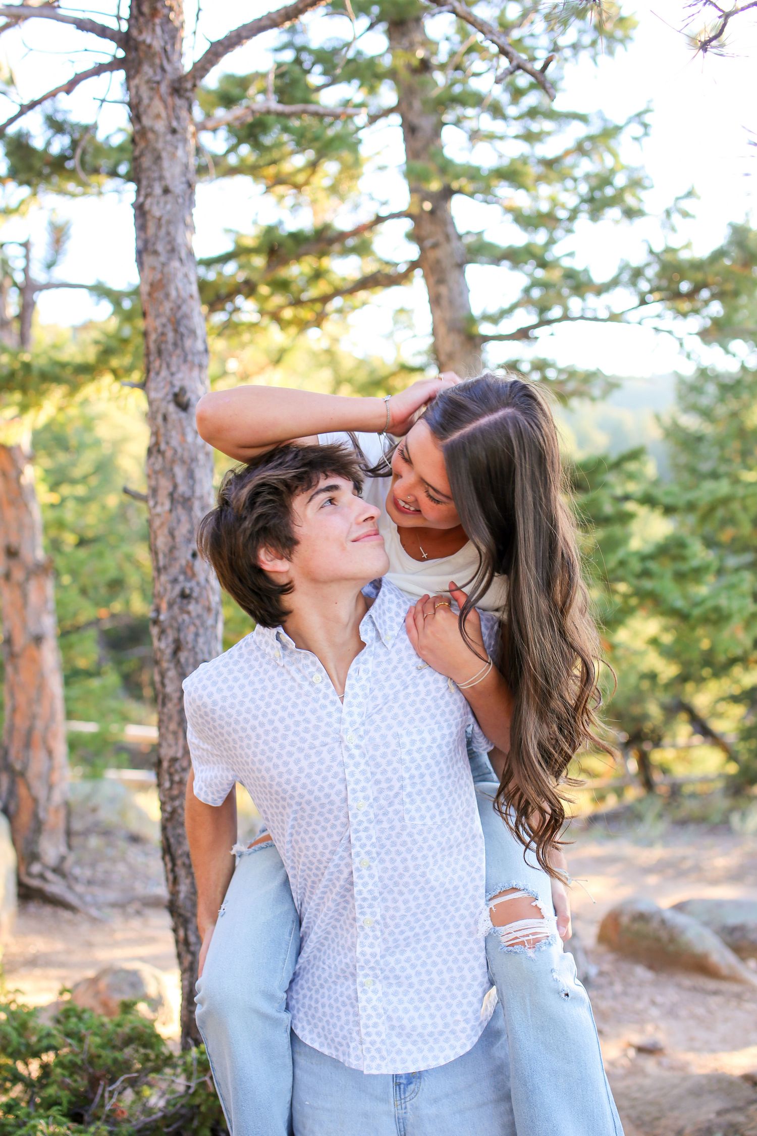 Couple shares intimate moment while laughing together in sunny forest setting.