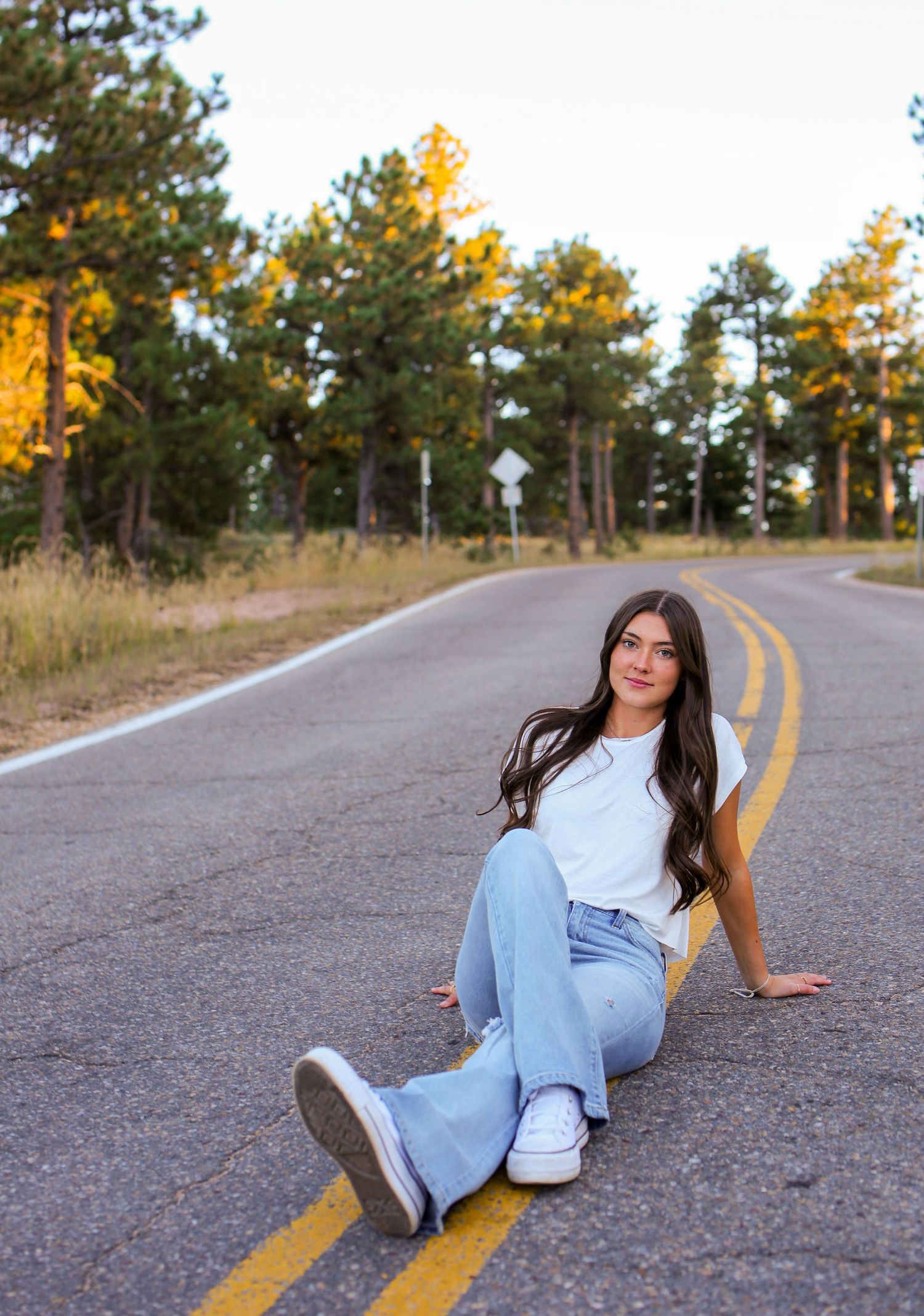 Someone in relaxed pose on mountain road wearing white t-shirt and flared jeans at golden hour.
