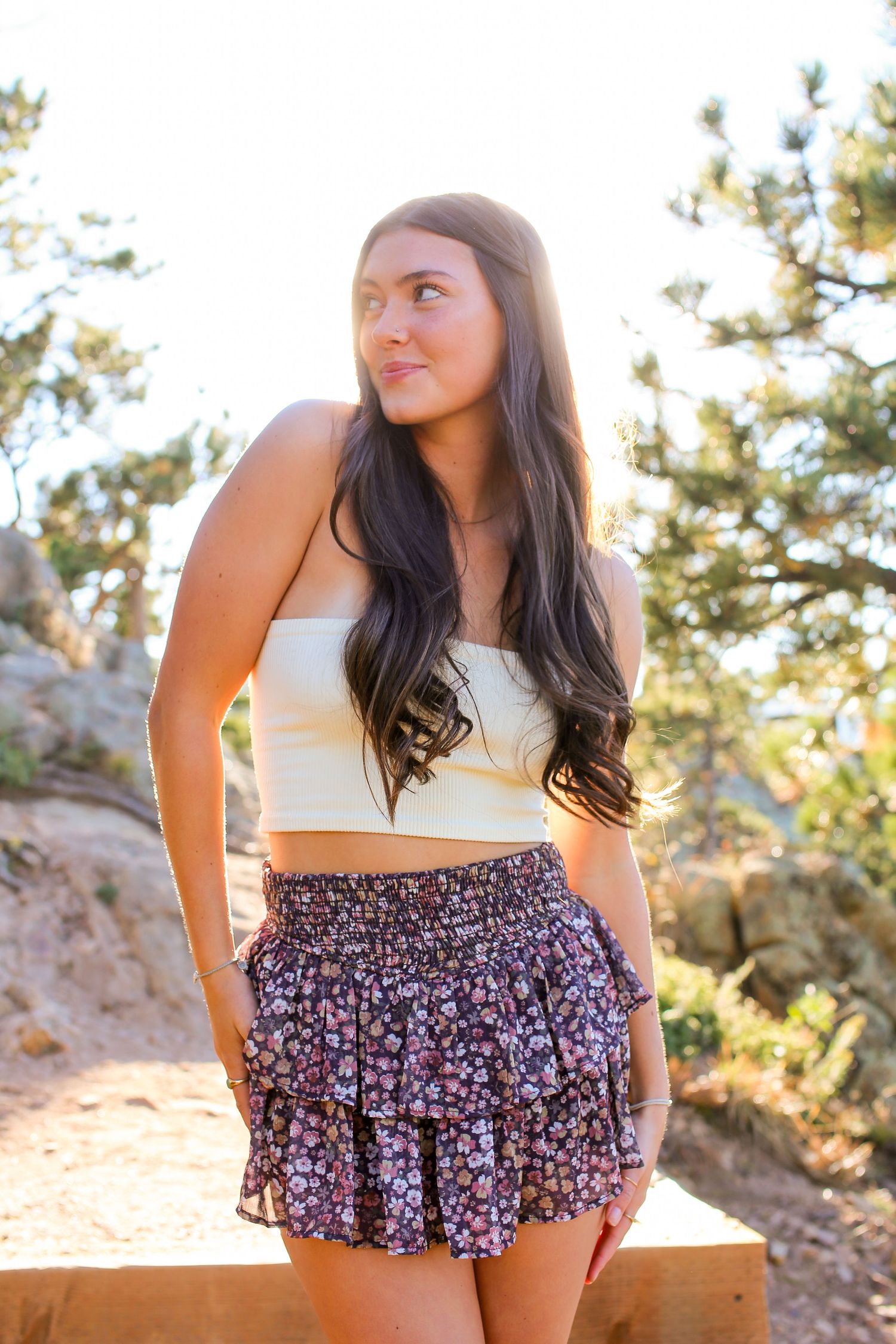 A person in a white crop top and floral shorts poses outdoors during golden hour.