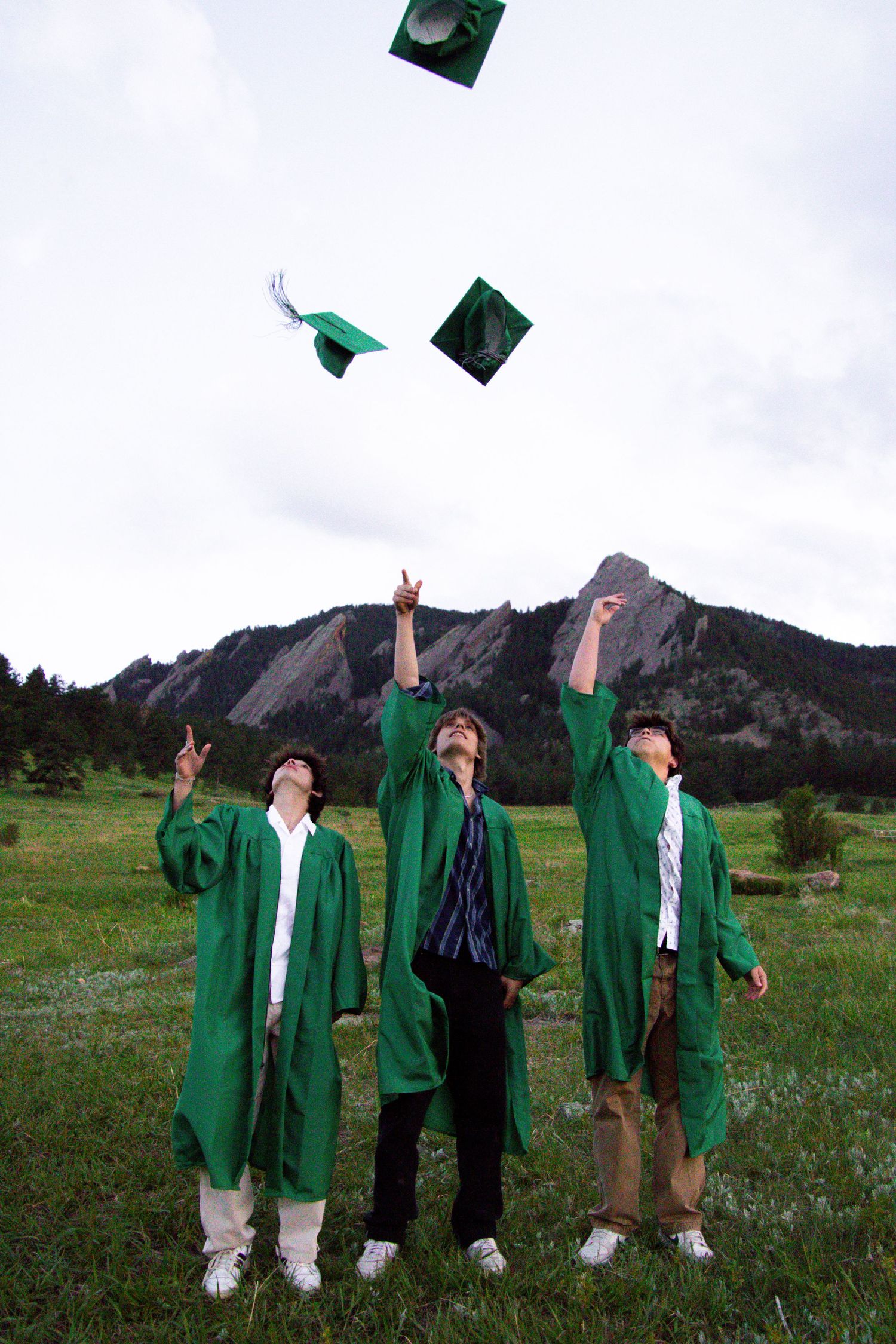 Graduates toss green caps in the air while celebrating in front of mountain landscape.