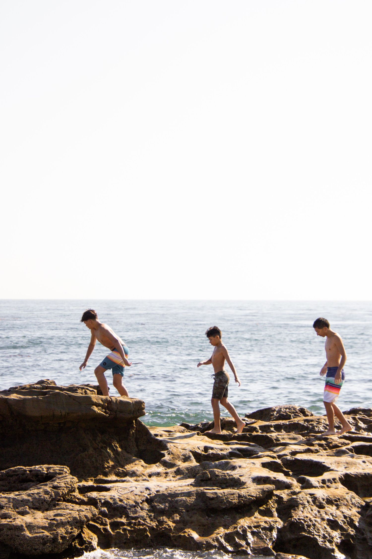 Group exploring rocky coastline and climbing over boulders near ocean waves.