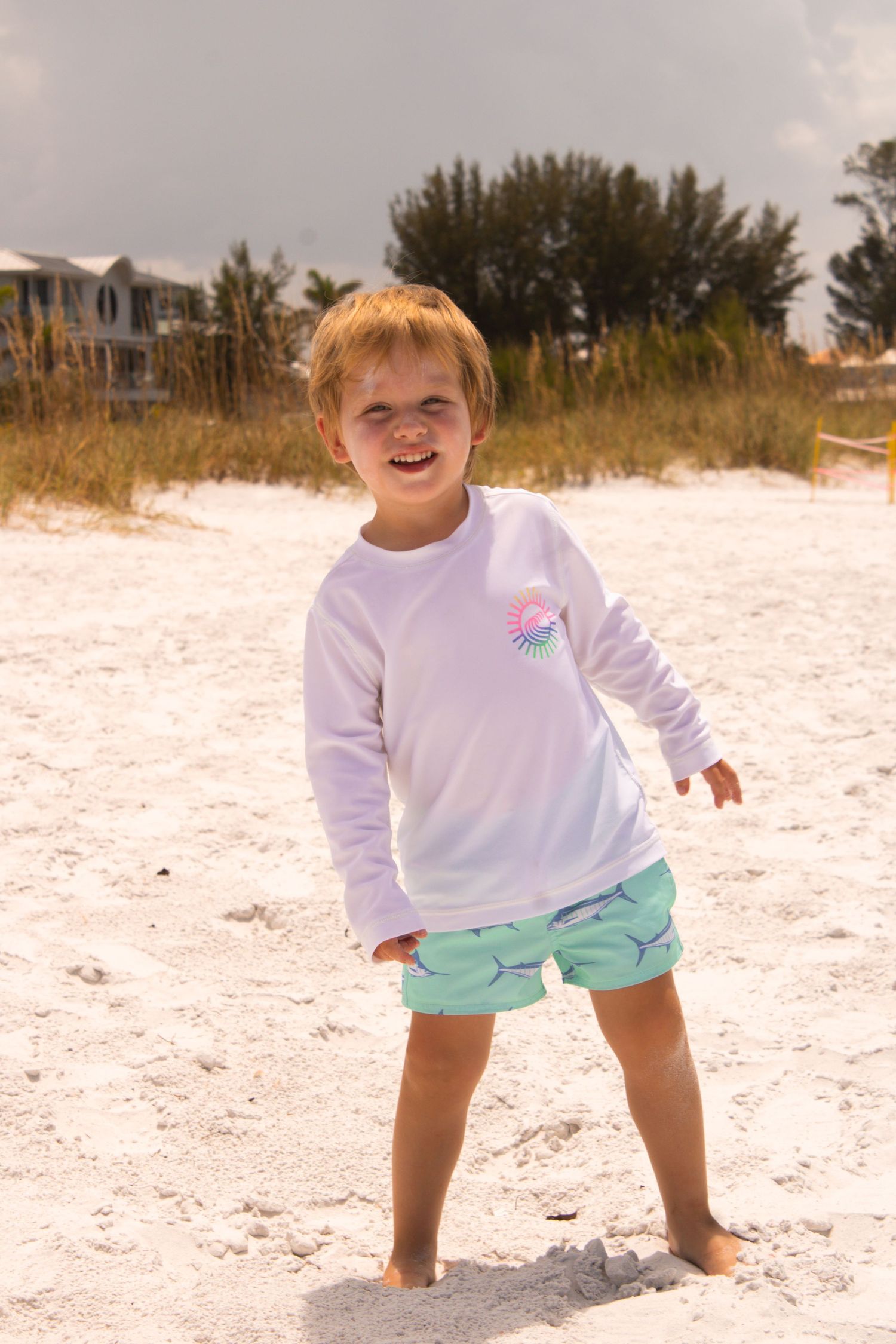 A child in beachwear explores white sandy shores near coastal homes.