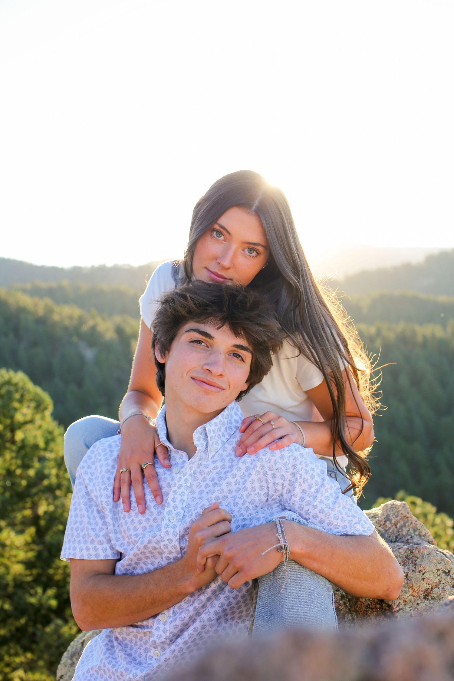 Couple embracing outdoors during golden hour with mountain landscape in background.