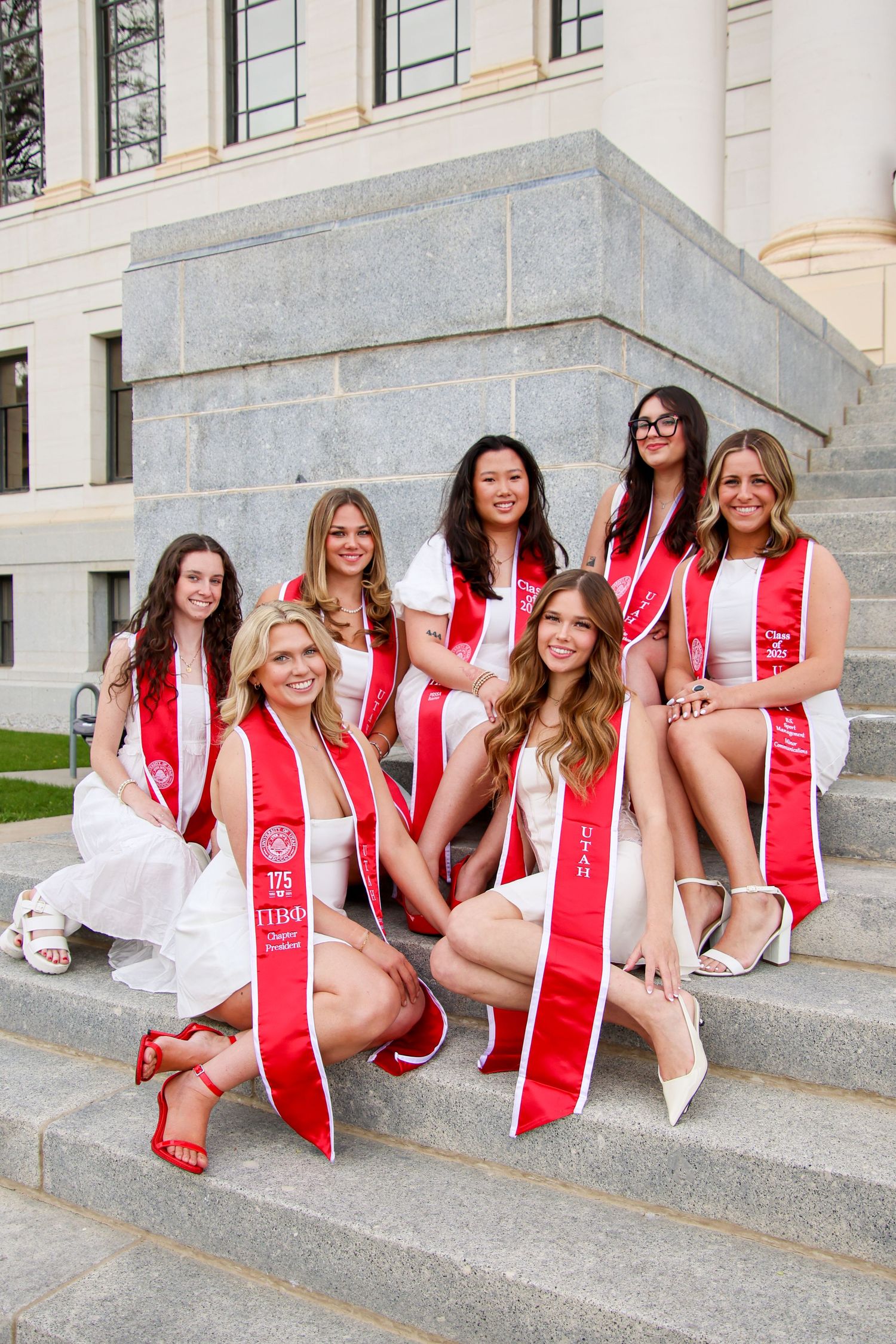 Graduates in matching attire pose casually on stone steps of a university building.